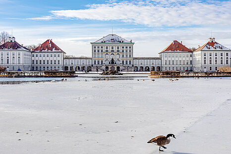 The photo shows the Nymphenburg castle with snow and partially frozen pond