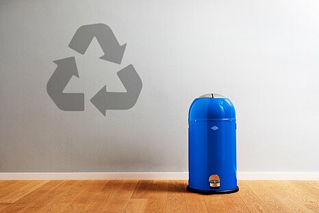 The photo shows a blue trash can to the right, and a recycling symbol to the left